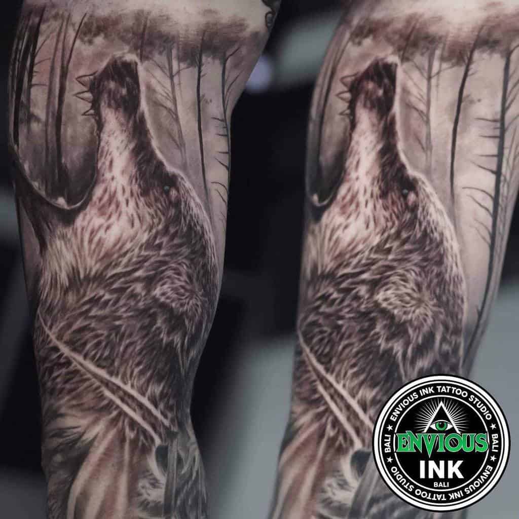 Realistic wolf tattoo on arm, howling in a dense forest, captures the wild essence perfectly