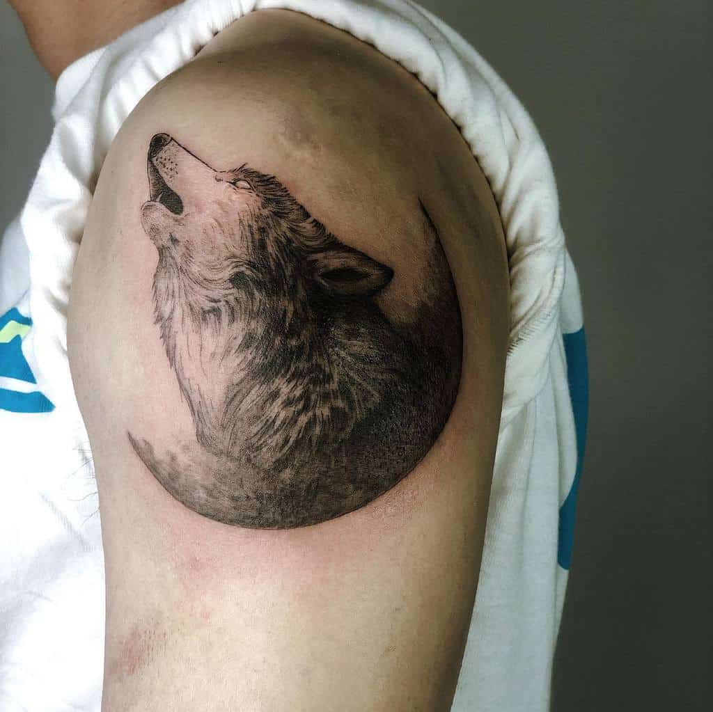 A detailed wolf tattoo on an upper arm, capturing the wolf howling with realistic shading
