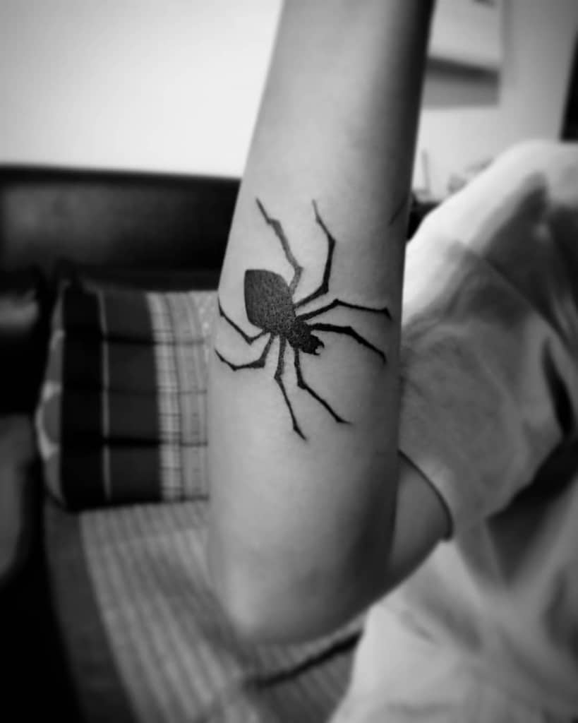 Minimalist black-ink tattoo of the Phantom Troupe spider emblem from Hunter x Hunter, displayed on the forearm