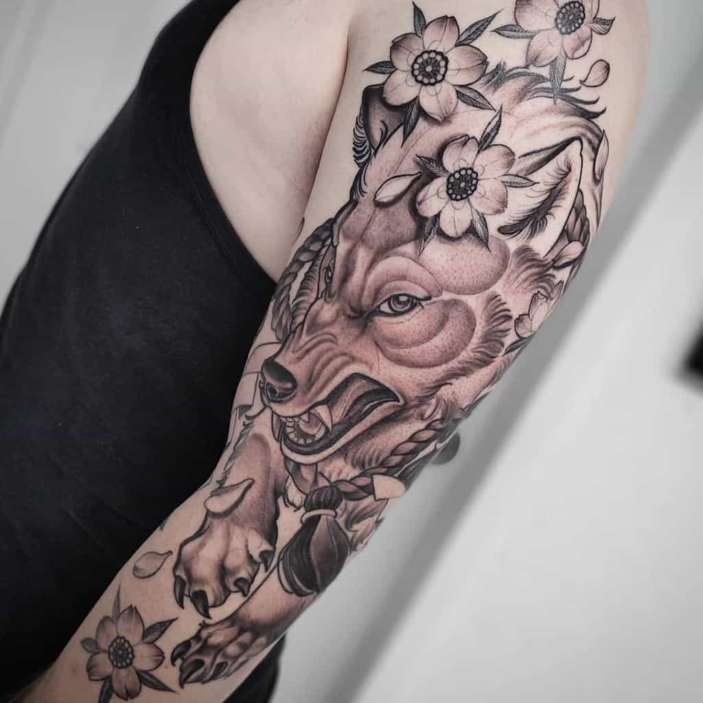 Arm tattoo of a detailed wolf, elegantly intertwined with floral elements in black and gray shading, drawing inspiration from Japanese artistry