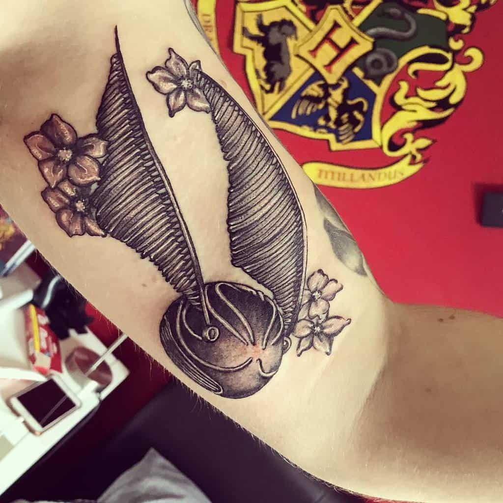 Tattoo of the Golden Snitch on an arm with flowers