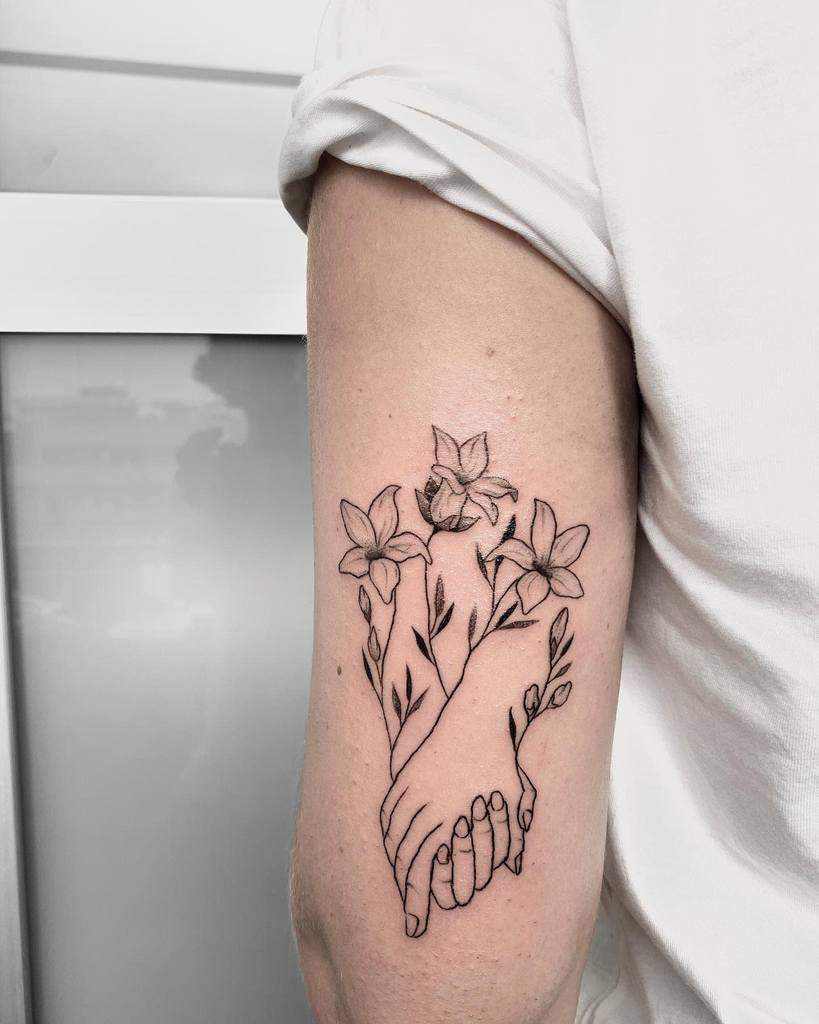 Tattoo on arm of two hands holding, with jasmine flowers and leaves intertwined around them