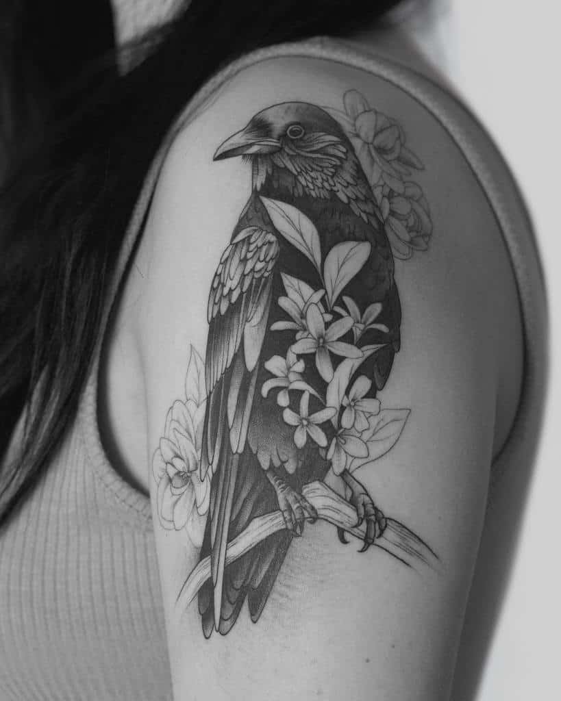 Black and white tattoo of a bird with jasmine flowers on an upper arm