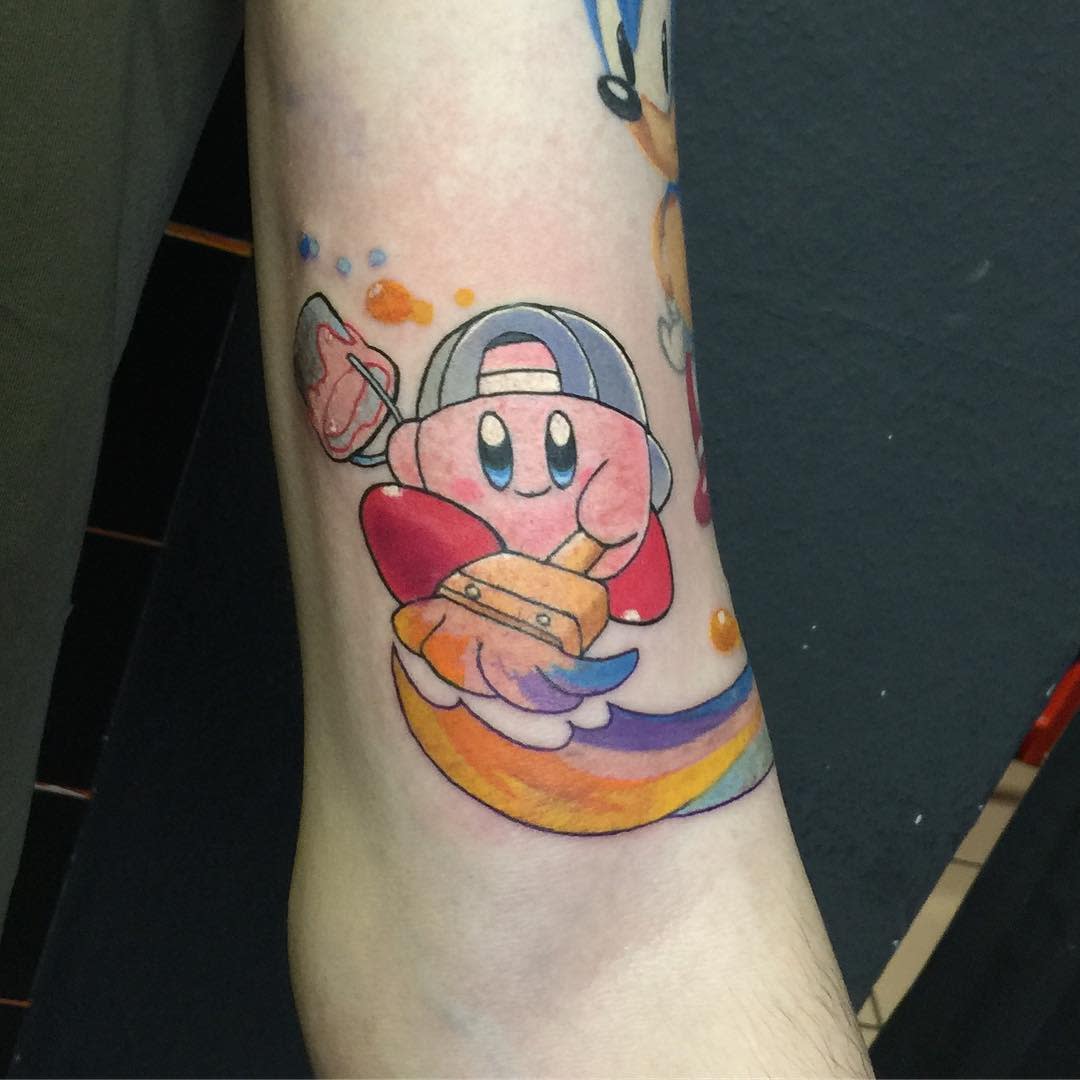 Kirby tattoo wearing a cap, painting a rainbow trail with a brush and bucket, a colorful and playful design with vibrant shading