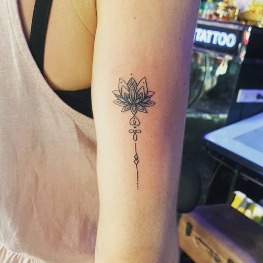 Unalome tattoo with a detailed lotus on the upper arm, symbolizing spiritual growth, enlightenment, and the journey to inner peace.
