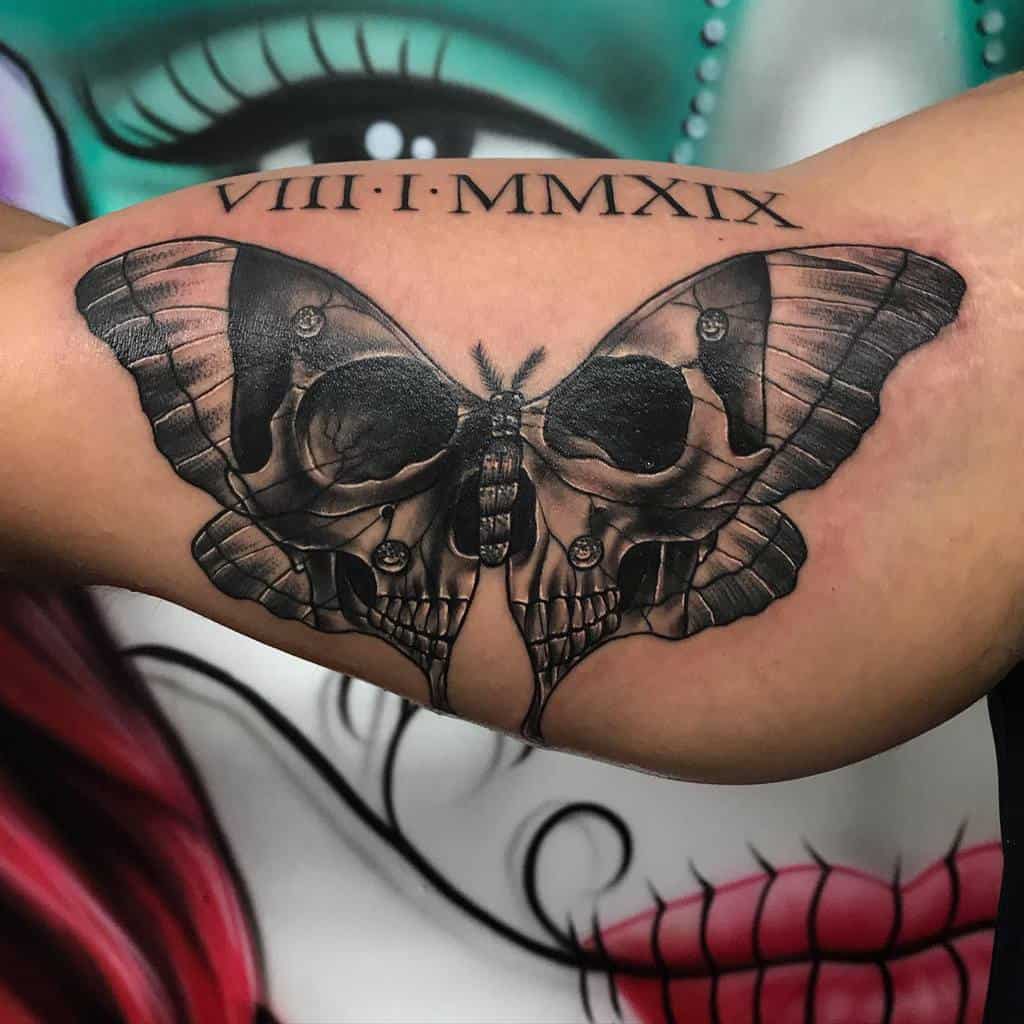 A black and grey tattoo of a Luna Moth with skull patterns on its wings, accompanied by a Roman numeral date (VIII I MMXIX)