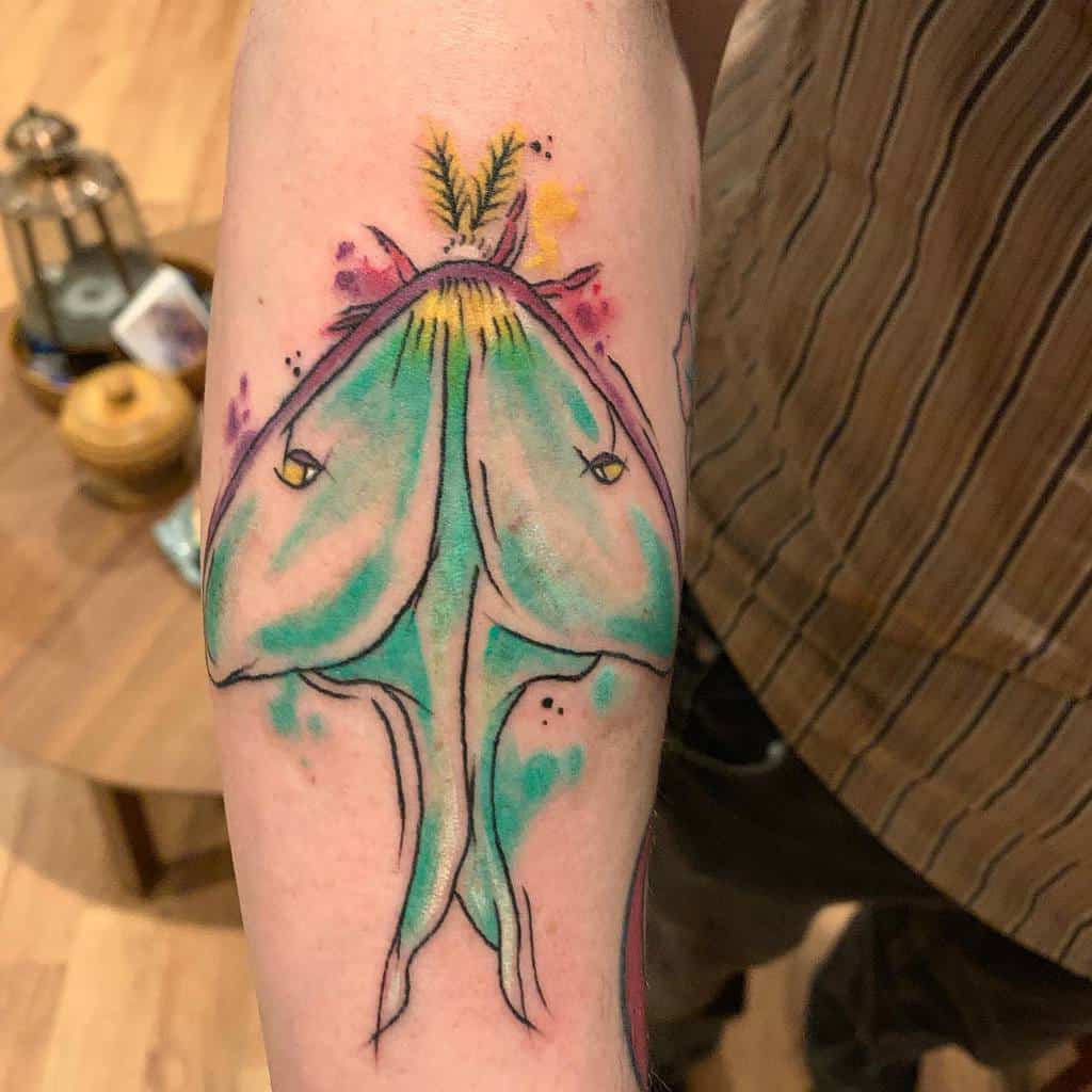 A colorful Luna Moth tattoo with vibrant watercolors in green, yellow, and purple, featuring a whimsical design