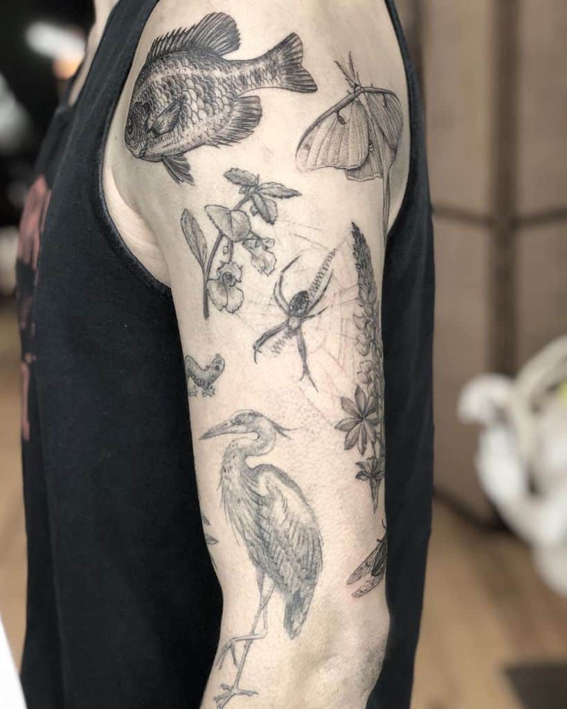 A black and grey tattoo featuring various nature elements, including a fish, Luna Moth, flowers, a heron, and a spider