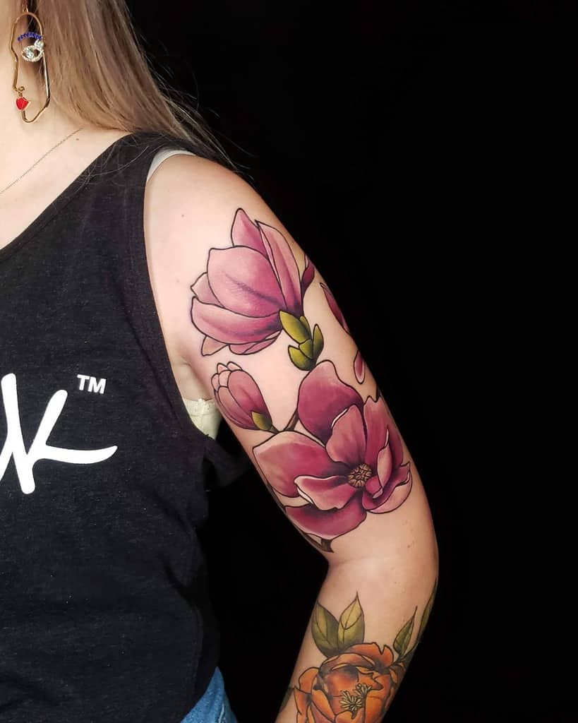 A woman with vibrant floral tattoos, featuring elegant magnolia blooms, graces her arm