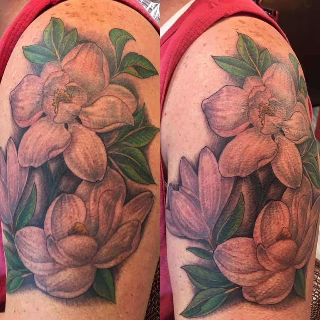 A stunning arm tattoo of delicate pink magnolia flowers intertwined with vibrant green leaves