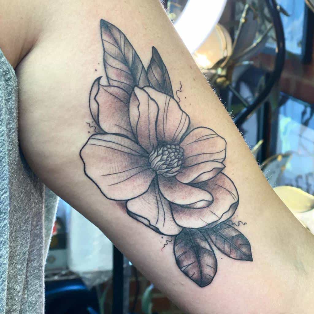Tattoo of a large magnolia flower with leaves elegantly gracing an upper arm