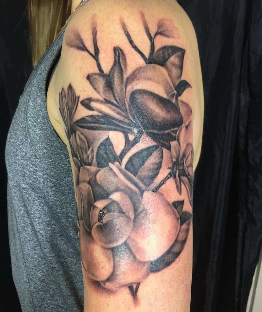 A black and gray floral tattoo featuring magnolias elegantly sprawls across an upper arm