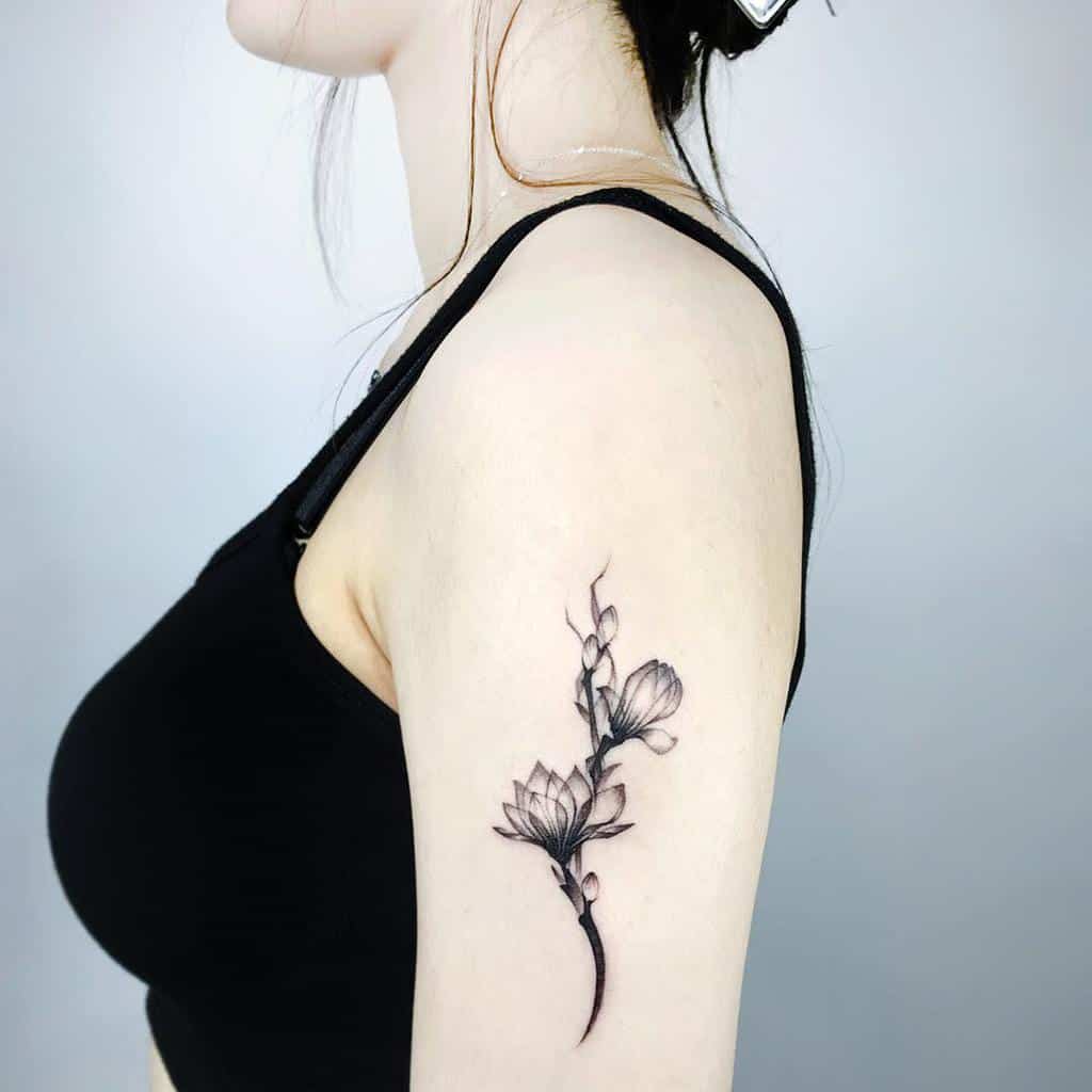 A woman with a black floral tattoo, featuring an intricate magnolia design, adorns her upper arm
