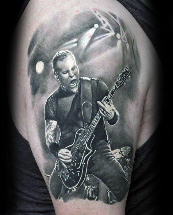 Realistic upper arm tattoo of James Hetfield playing guitar on stage, with detailed lighting and expressive performance captured in black and grey.