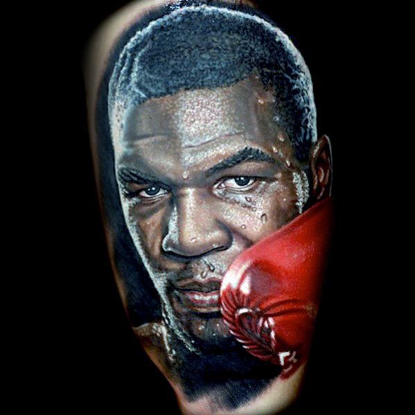 Realistic tattoo of legendary boxer Mike Tyson, featuring his intense gaze, red boxing glove, and signature determination