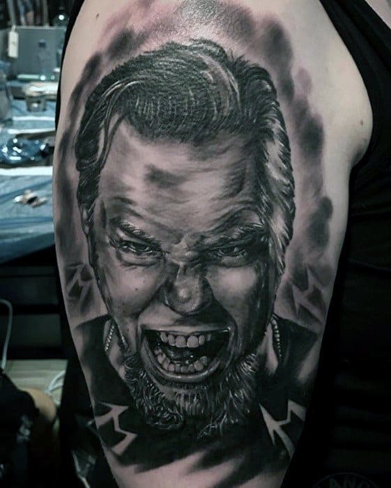 Intense black and grey upper arm tattoo of James Hetfield screaming, with dramatic shading and Metallica M logos in the background.