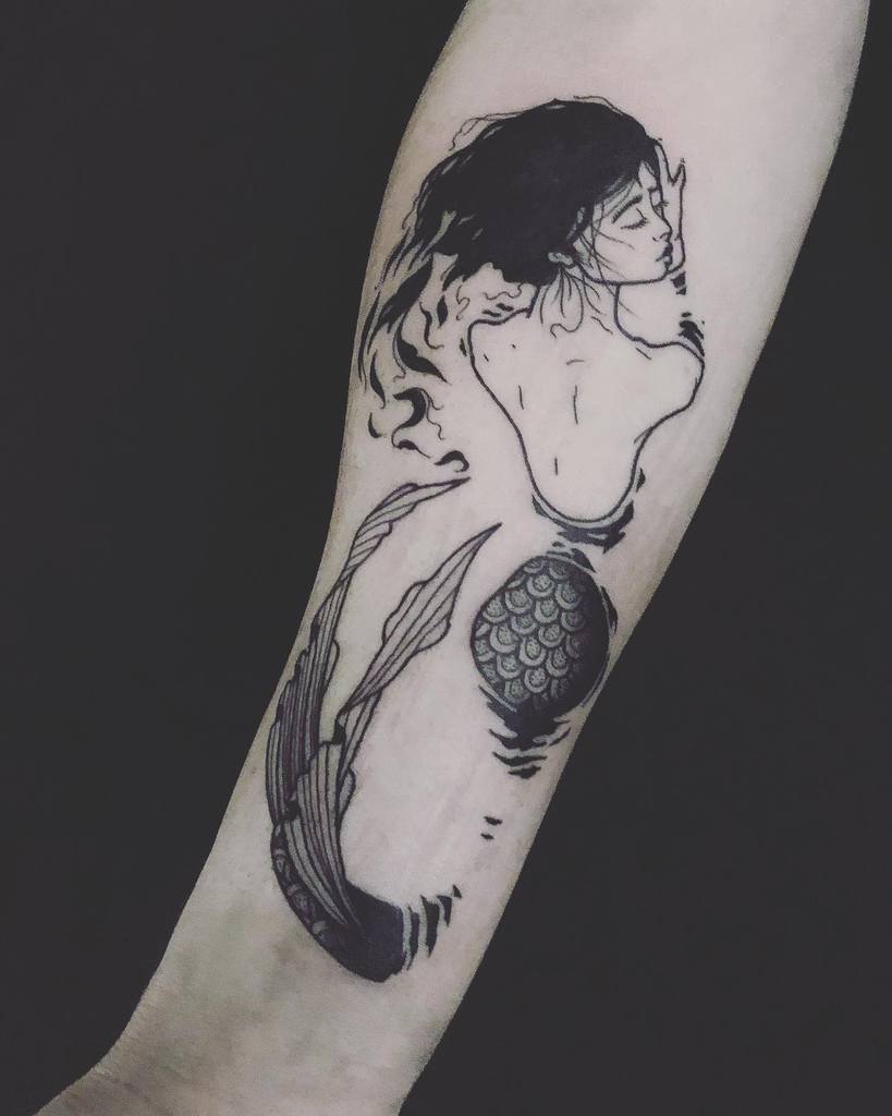 Black and grey tattoo of a mermaid with long flowing hair, gazing back with a delicate expression, featuring fine line details and shading.