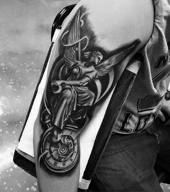 A black and grey tattoo on the upper arm featuring an angel holding a rope, with a clock design incorporated into the artwork.
