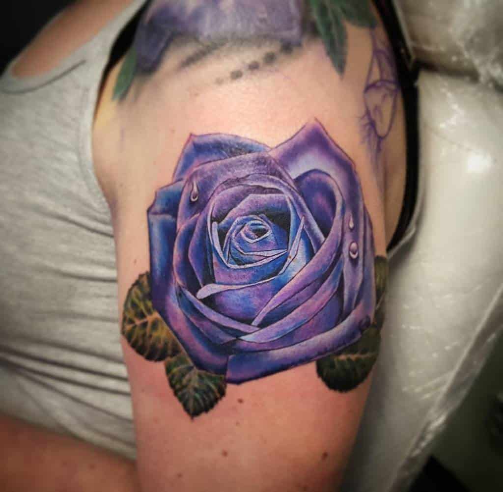 A stunning tattoo featuring a lifelike purple rose adorned with delicate water droplets graces the person's upper arm