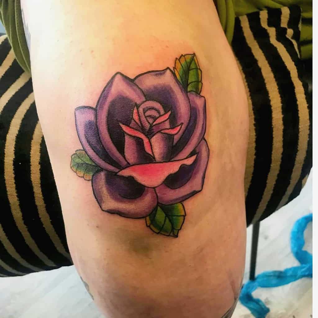 A stunning tattoo featuring a vibrant purple rose adorned with lush green leaves graces the arm