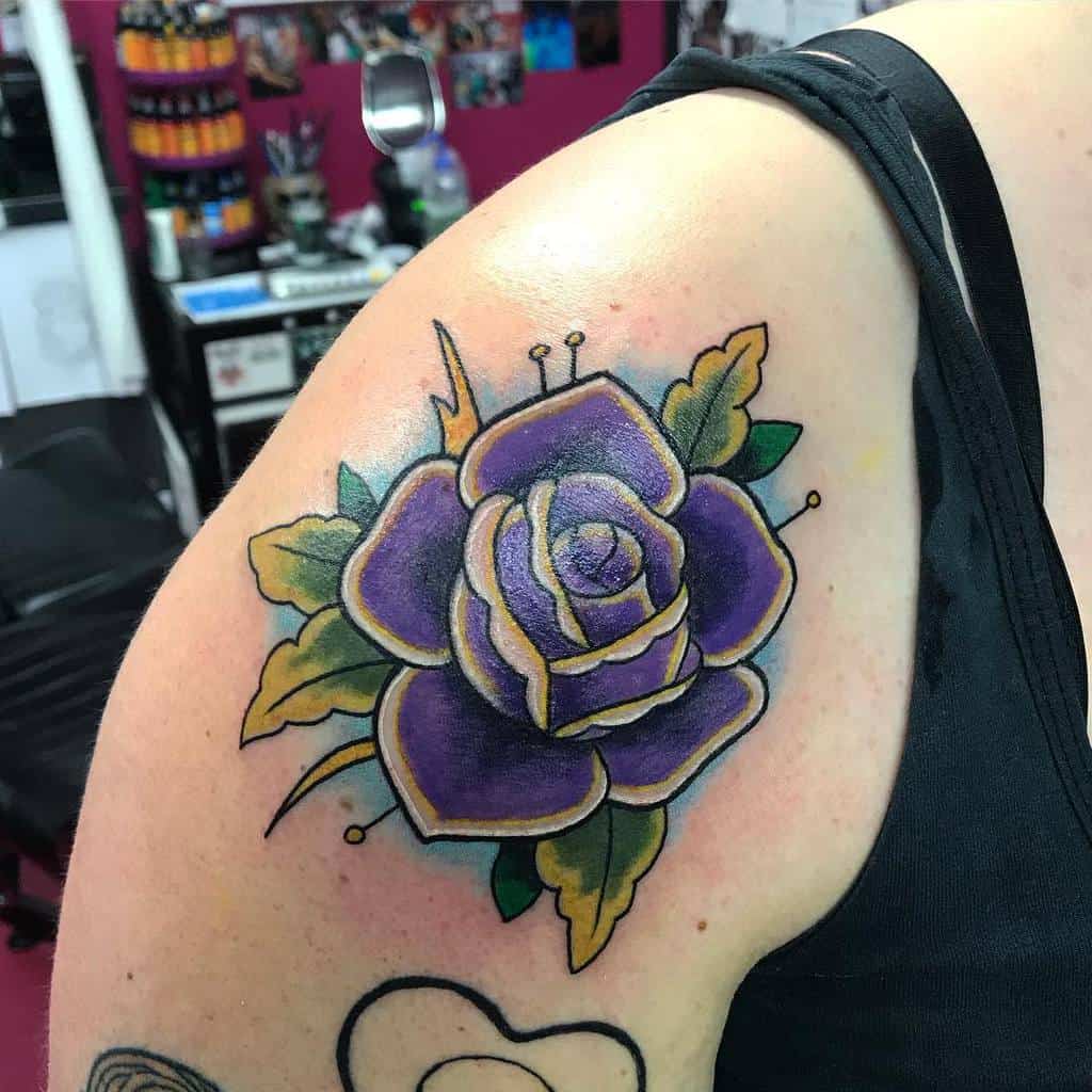 A delicate tattoo graces the upper arm, showcasing a stunning purple rose with lush green leaves, adding an elegant touch to the skin