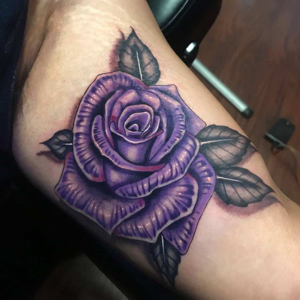 A stunning tattoo showcases a vibrant purple rose with lush green leaves elegantly adorning the arm