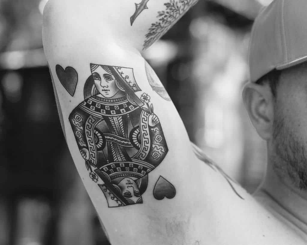 Tattoo of a Queen of Spades card on a person's inner arm, next to a heart symbol