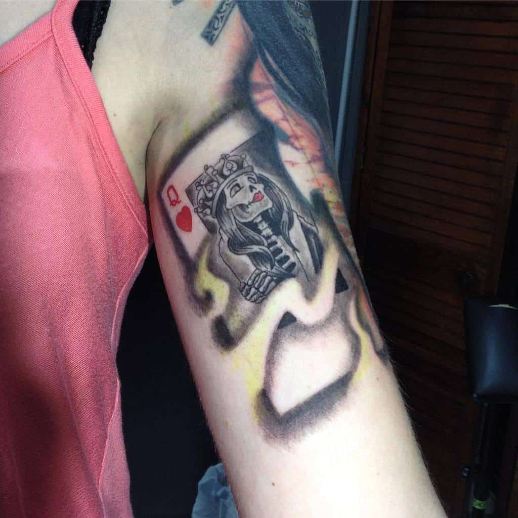 Close-up of a playing card tattoo on an arm, featuring a king of hearts with a unique design