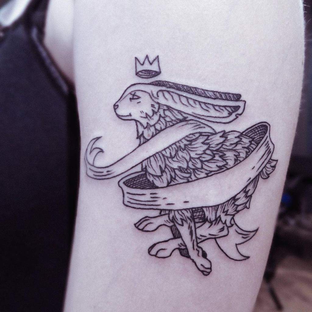Tattoo of a rabbit with a ribbon swirling around it, wearing a small crown