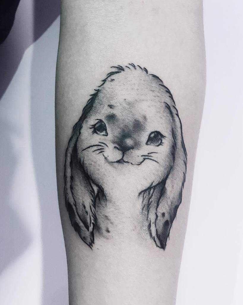 Stylized tattoo of a rabbit with a human body, wearing a skirt and standing in a serene pose, surrounded by minimalistic plants