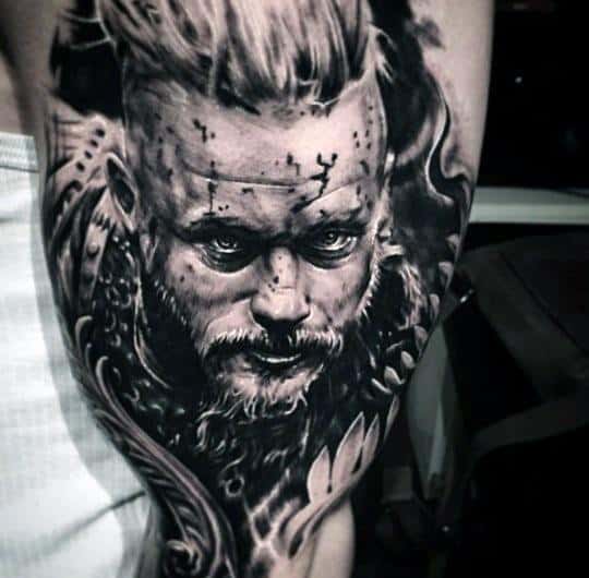 Detailed Ragnar Lothbrok tattoo on upper arm, featuring his intense gaze, battle scars, and armor details.