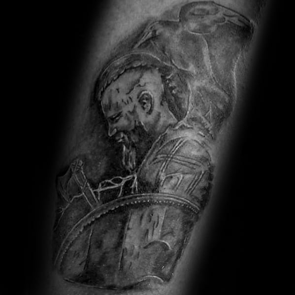 Black-and-white tattoo of a warrior with braided hair and armor, gazing downward