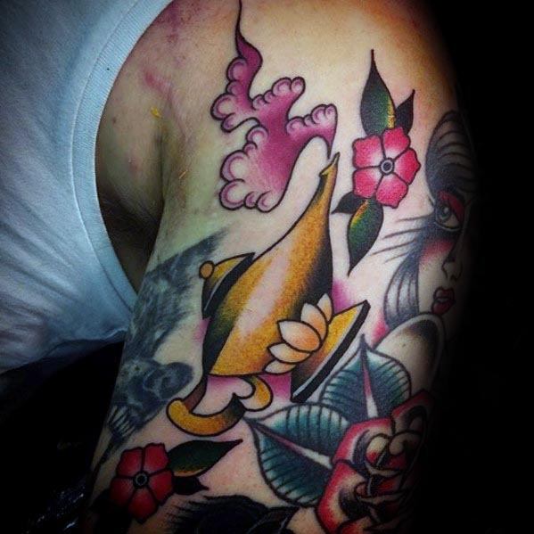 Vibrant tattoo of a golden genie lamp surrounded by flowers, leaves, and decorative smoke on the arm