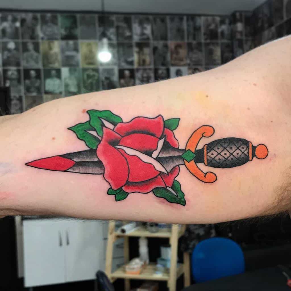 Tattoo of a dagger piercing through a red rose on an upper arm