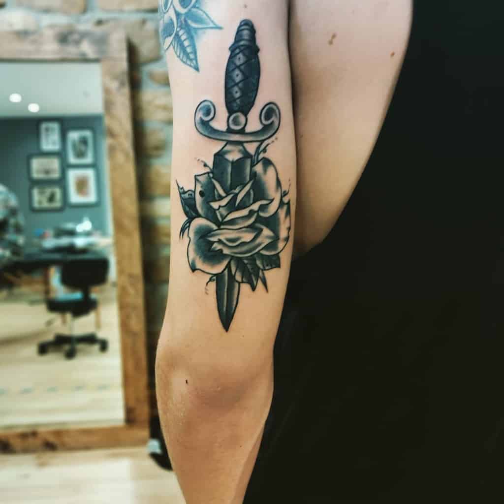 Tattoo of a dagger piercing a rose on a man's upper arm