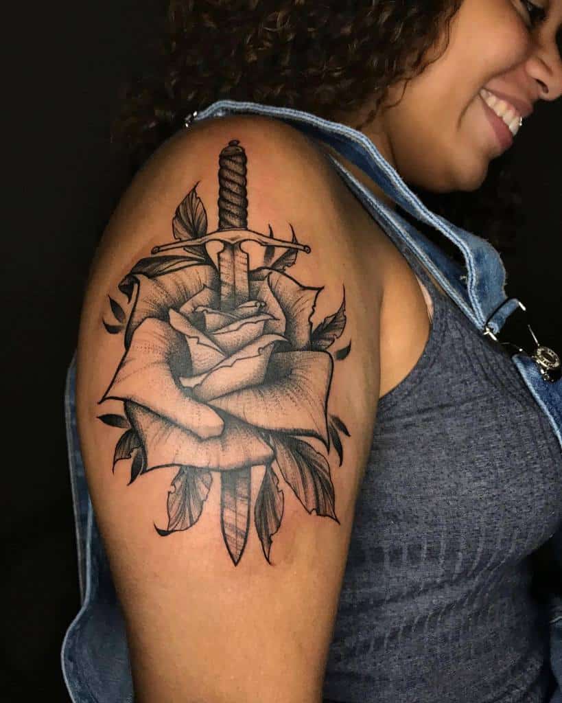 Tattoo of a dagger through a rose on a woman's upper arm