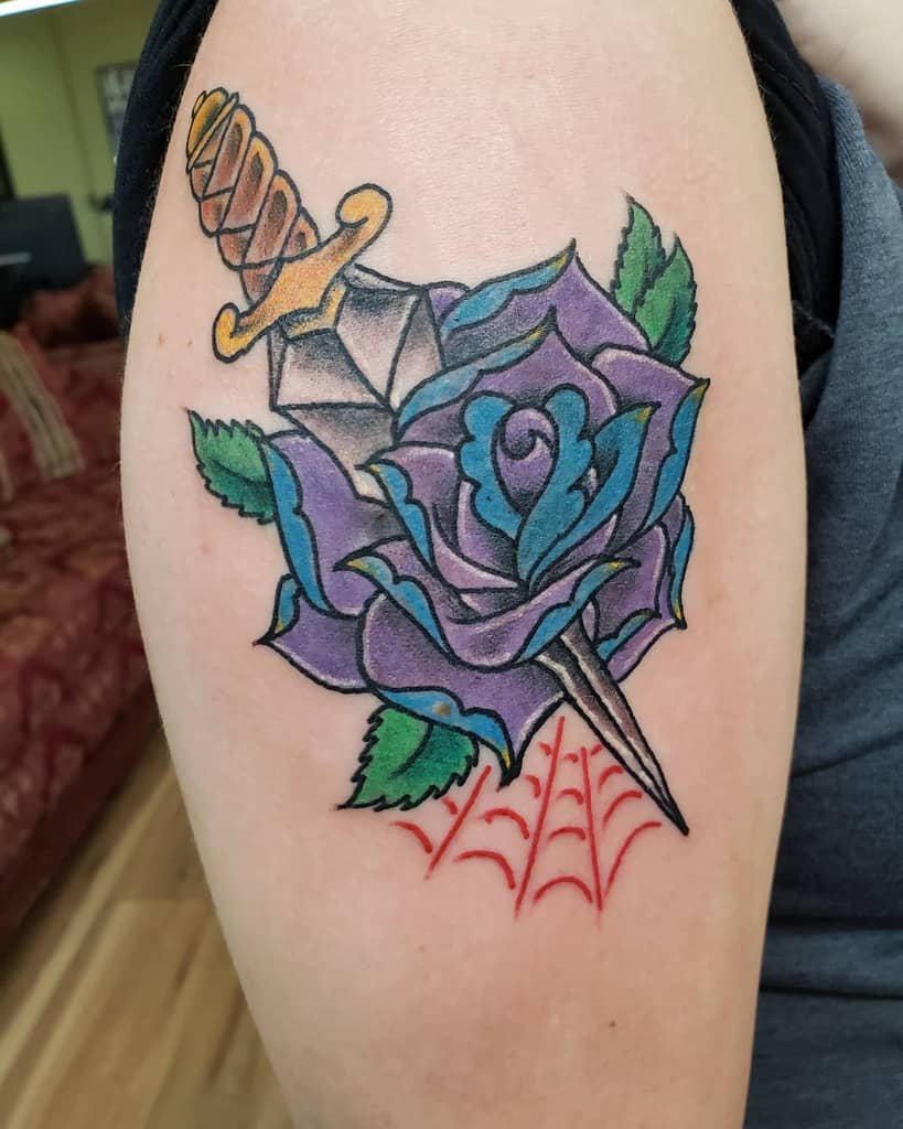 Tattoo of a dagger through a blue rose with red webbing on an upper arm