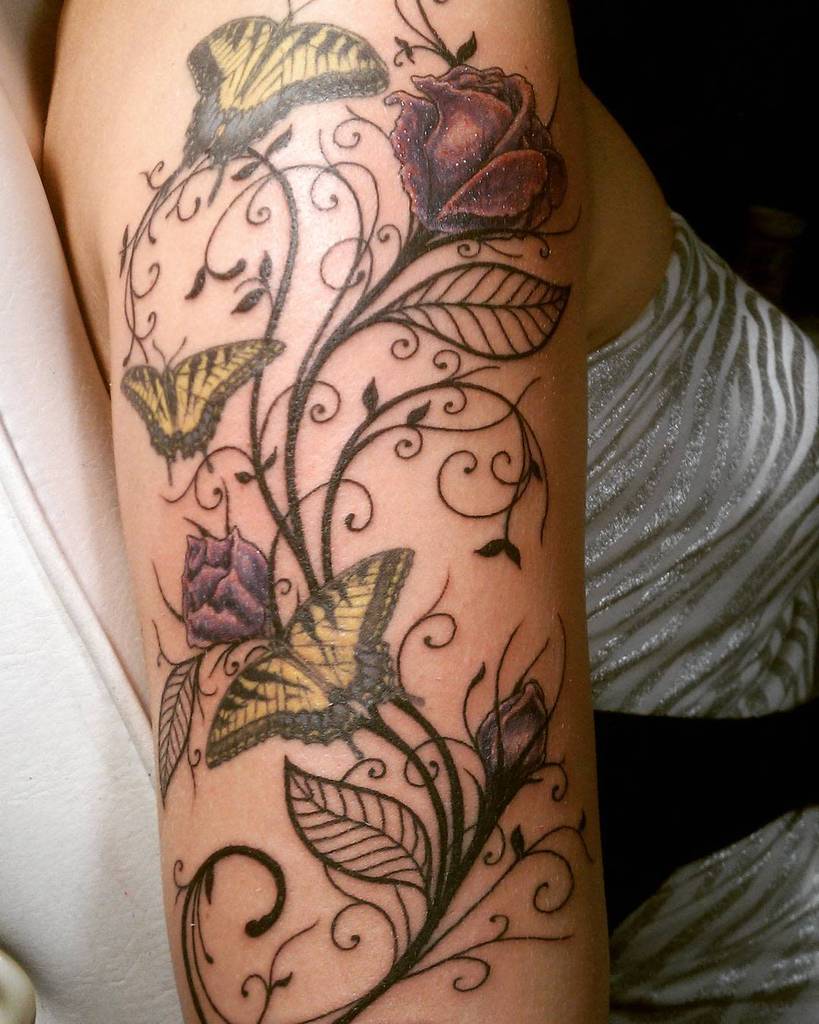 Colorful tattoo featuring vibrant roses, swirling vines, and detailed yellow butterflies on the arm