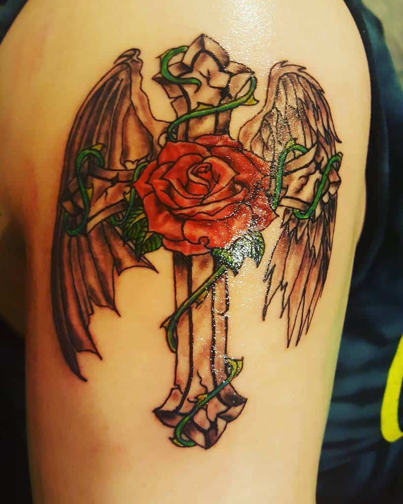 Vivid tattoo of a red rose entwined with green vines around a stone cross, adorned with angelic wings on the arm