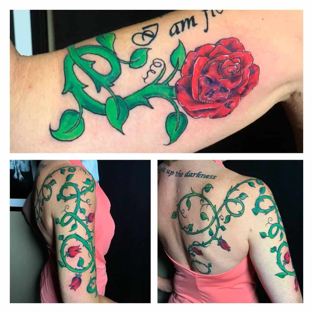 Intricate tattoo featuring vibrant red roses with green vines wrapping around the arm and extending across the back, accompanied by elegant script text