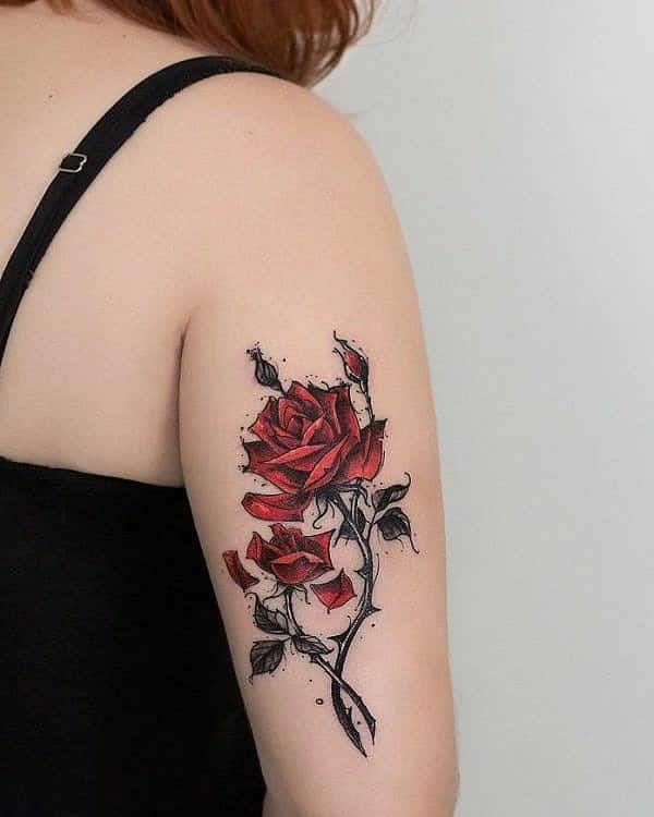 Elegant arm tattoo of a red rose with a twisting vine and buds, accented by subtle black ink splatters