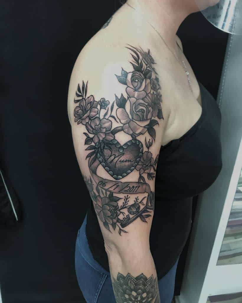 Black and grey tattoo featuring intricate roses, vines, and a heart design with the word 'Mom' and a date, spanning the upper arm and shoulder