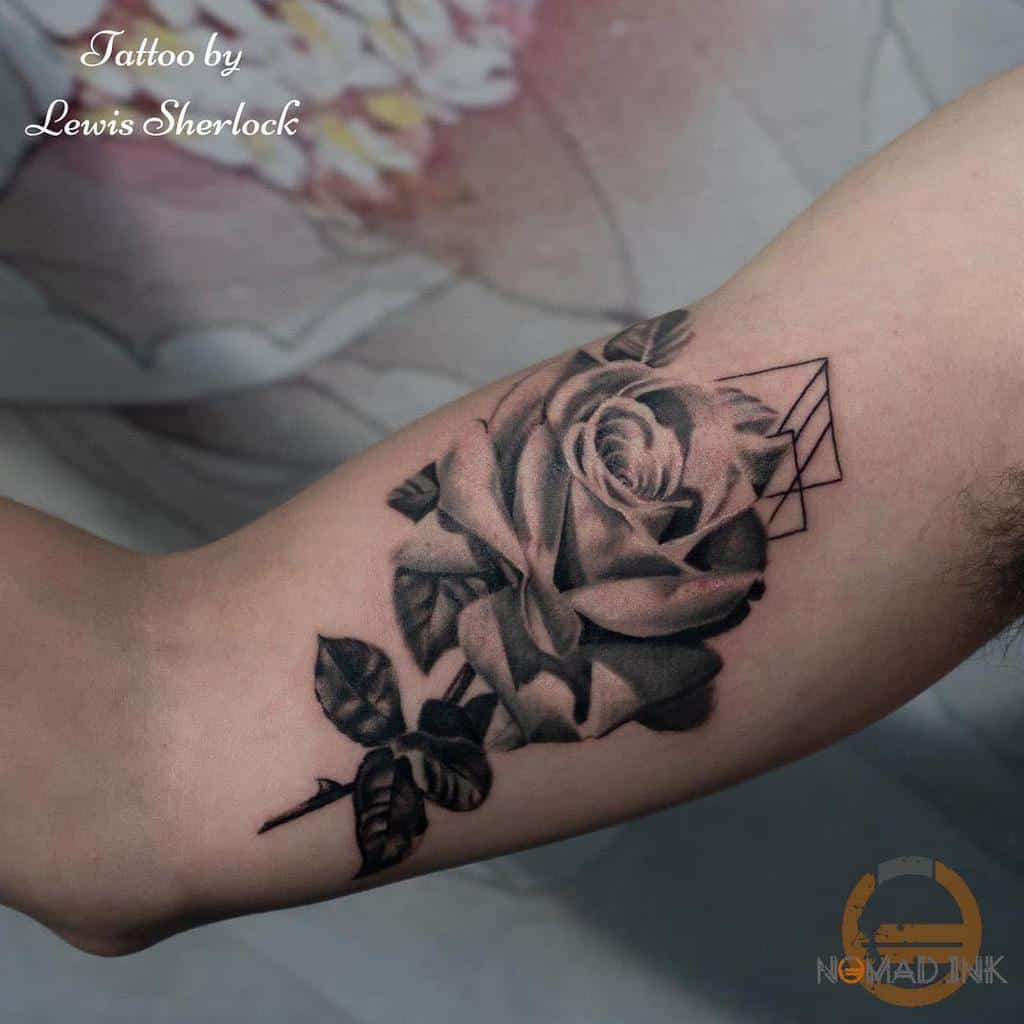 Black and gray rose tattoo on a person's inner arm, with geometric accents and a delicate stem adding elegance