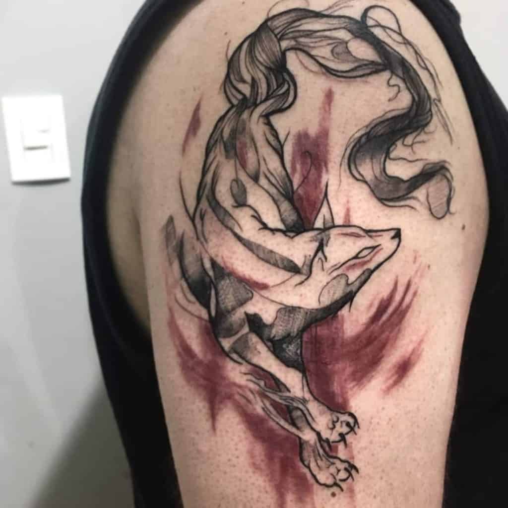 Dynamic Okami tattoo on the shoulder featuring Amaterasu with flowing ink-like strokes and bold red accents, creating a mystical, brushstroke effect