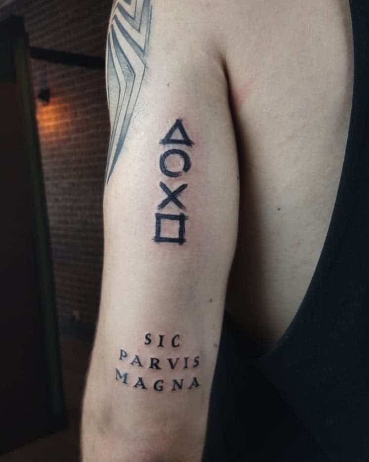 Upper arm tattoo with PlayStation symbols and "Sic Parvis Magna" text in black ink
