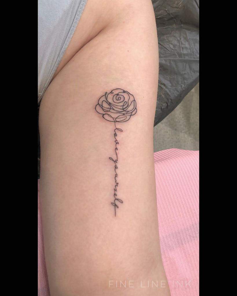A line art rose tattoo with the words "love yourself" forming the stem, elegantly placed on an arm