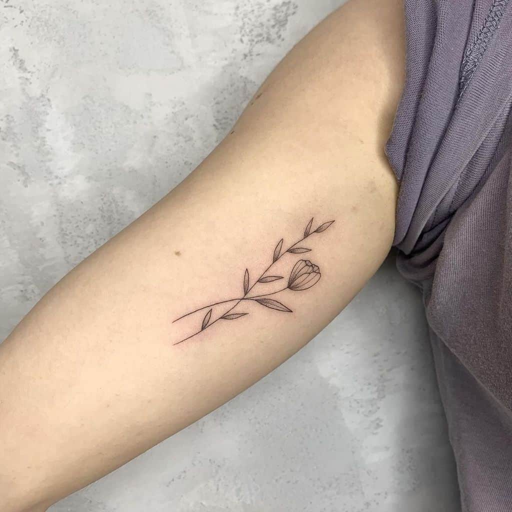 Minimalist tattoo of a flower and leaves on an upper arm
