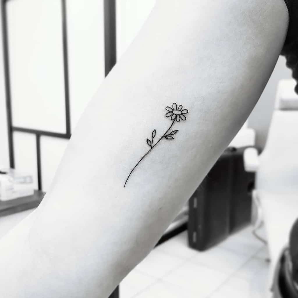A minimalist black ink flower tattoo on an inner arm