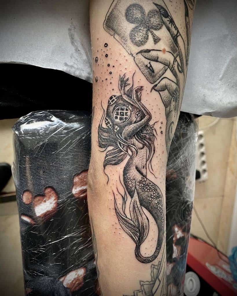 Detailed forearm tattoo of a mermaid wearing a vintage diving helmet, featuring intricate scales and flowing fins