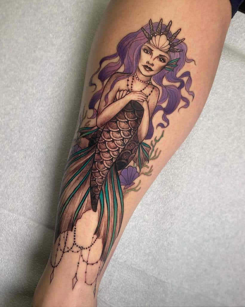 Tattoo of a crowned siren with long purple hair on a forearm, detailed with scales and aquatic elements
